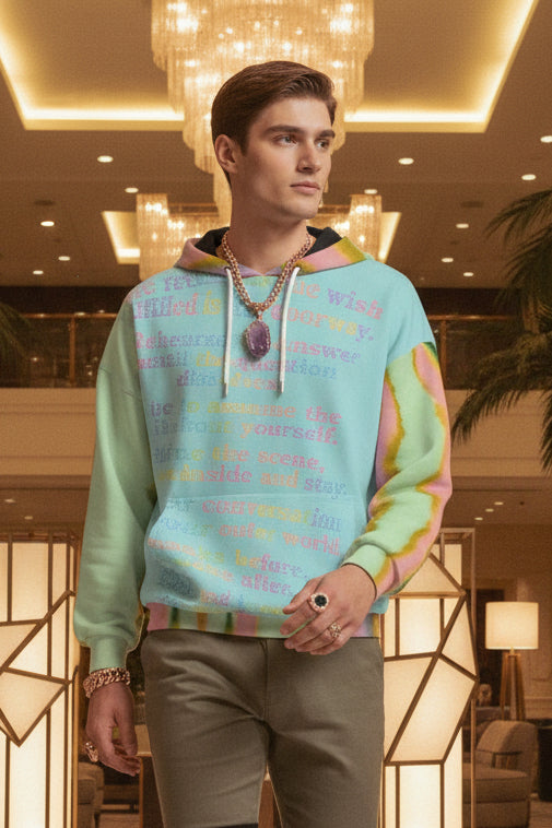 A man wearing a pastel rainbow tie-dye hoodie with colorful text on the front, set against a solid beige background.
